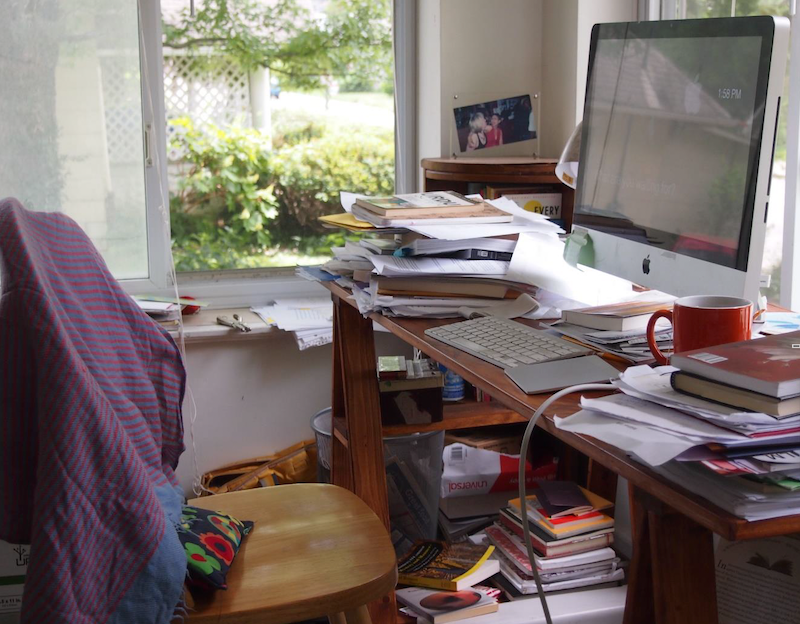 A messy wooden desk dominated by a large computer screen